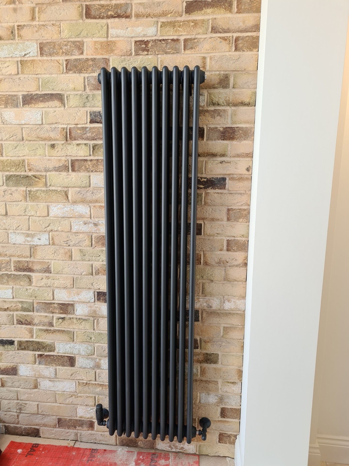 Grey column radiator mounted on exposed brick wall with copper connections