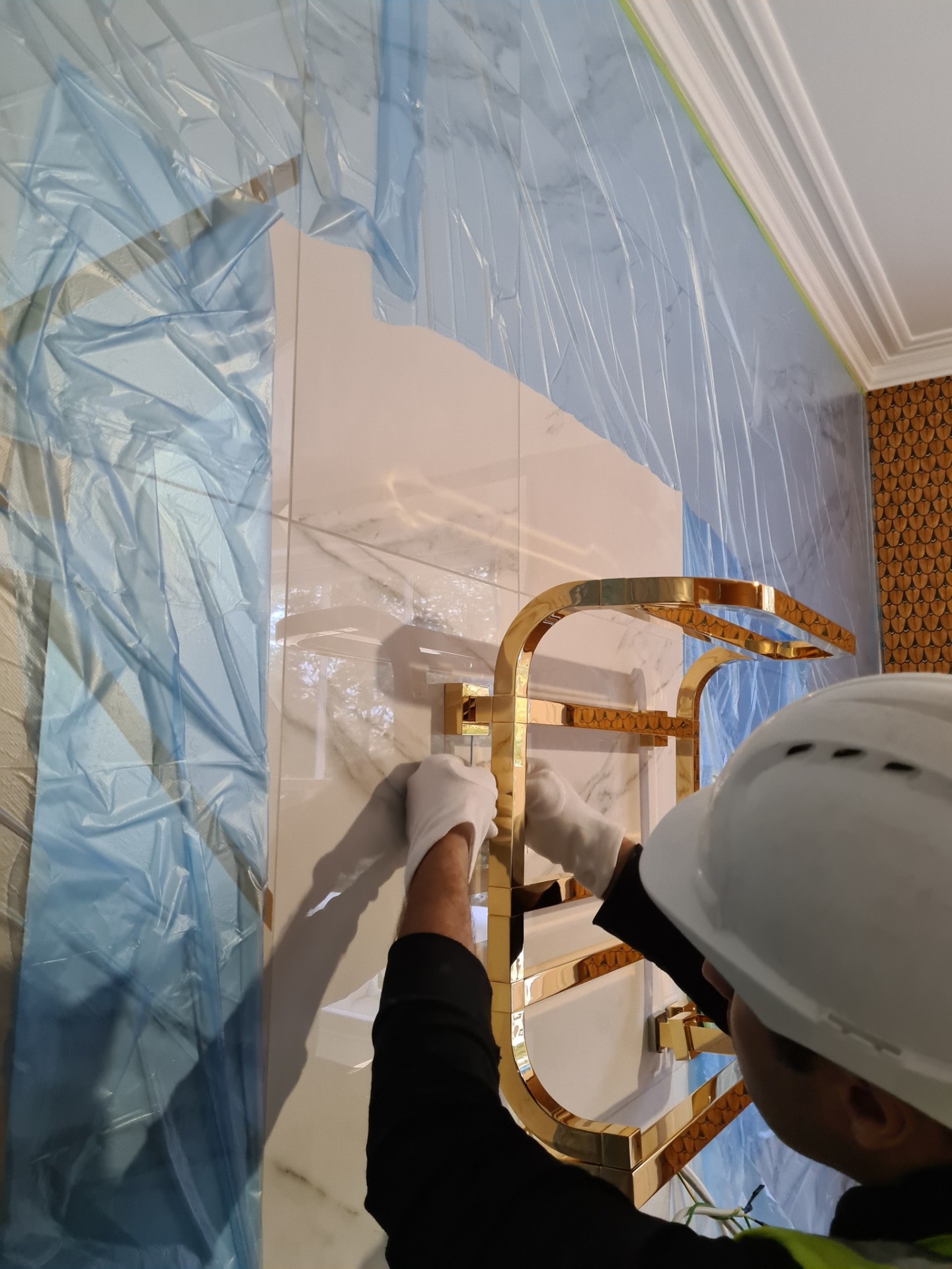 Engineer installing gold heated towel rail on marble-tiled bathroom wall