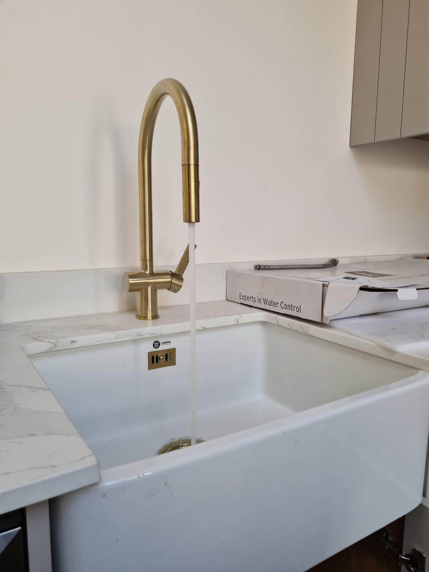Gold kitchen mixer tap running water into Belfast ceramic sink