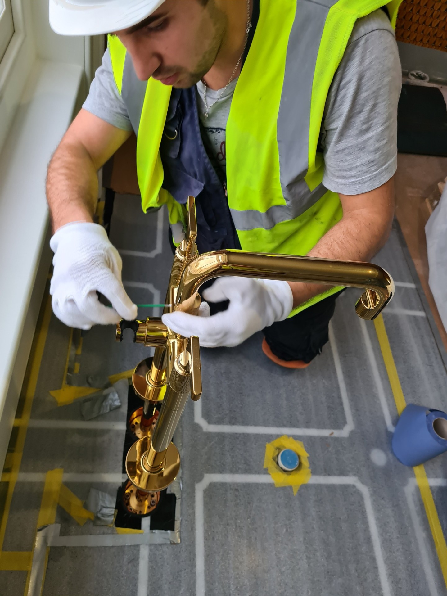 Plumber fitting a gold freestanding bath mixer tap with white gloves