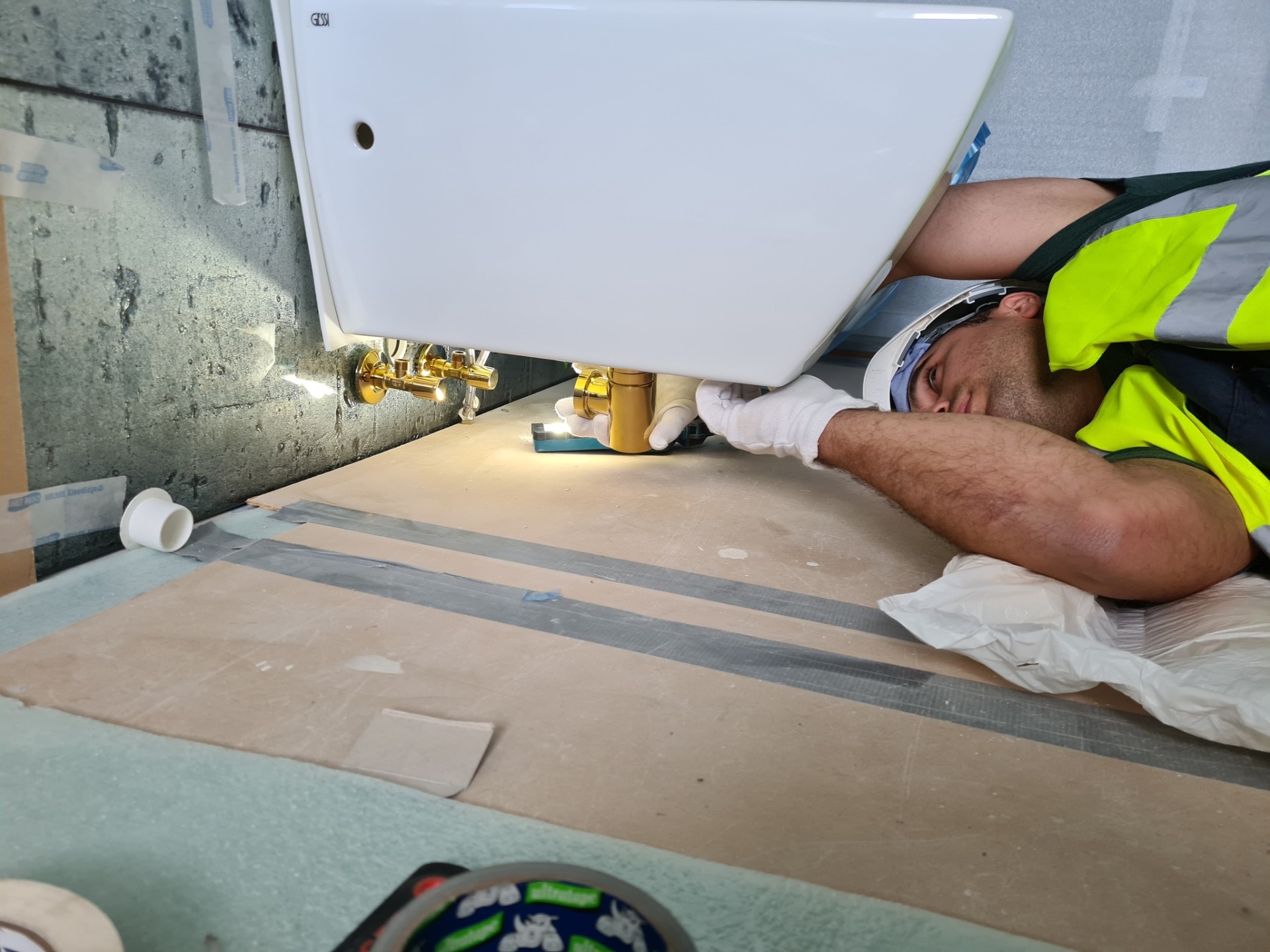 Plumber fitting gold bath waste trap beneath bathtub