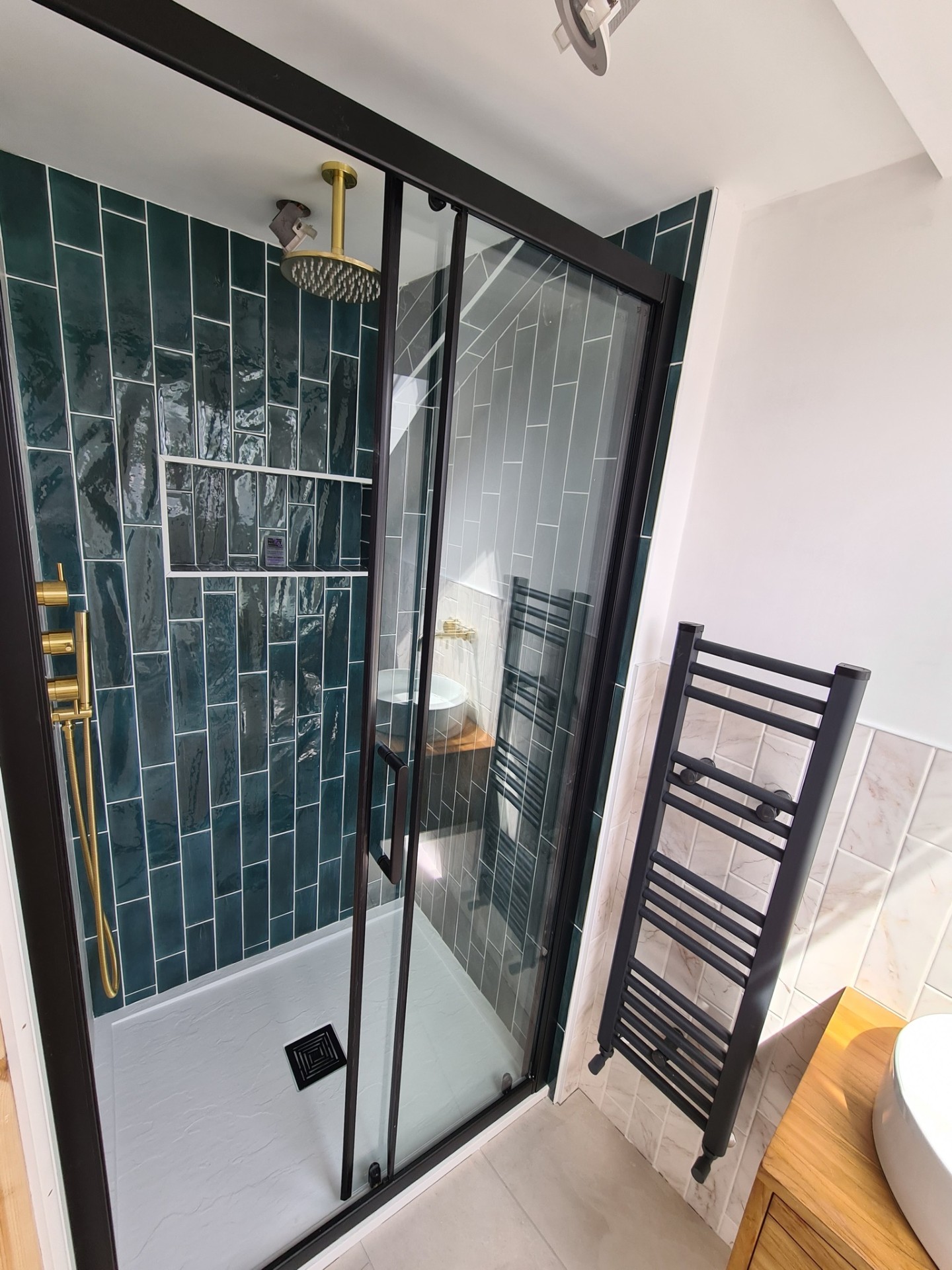 Shower enclosure with teal subway tiles, gold rainfall head and black frame